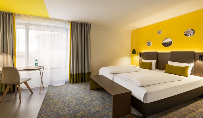A hotel room with bright yellow walls, a double bed, and a desk at Vienna House Easy, a hotel in Berlin, Germany