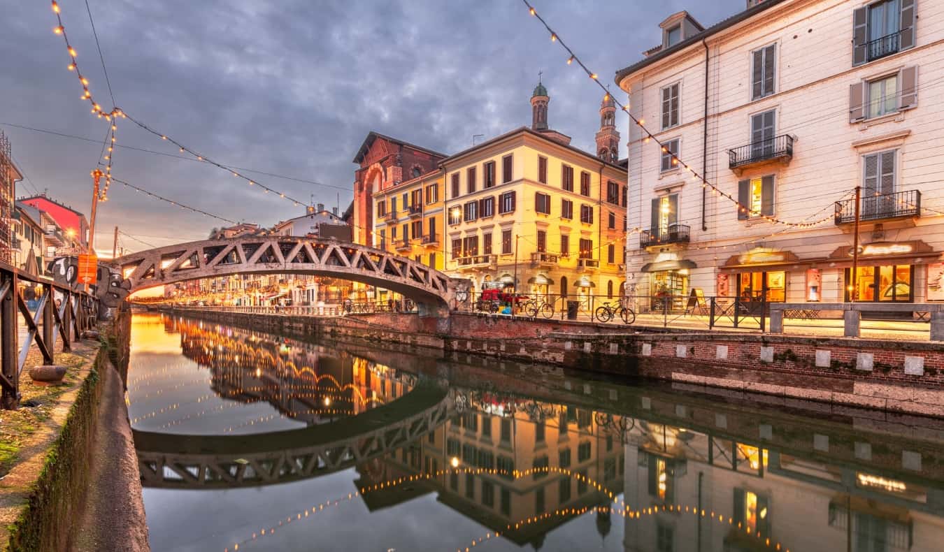 The picturesque and historic canals of the Navigli neighborhood with string lights hung over them in the twilight of the evening in Milan, Italy