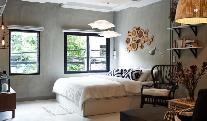 Double bed in hotel room with large windows, brushed concrete windows and wooden accents on walls at House of Phraya Jasaen hotel in Bangkok, Thailand