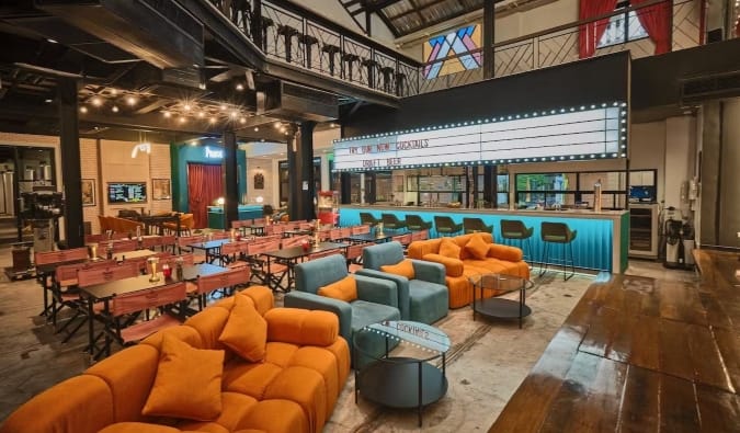 Tables and comfortable chairs are set up in front of the cinema bar stage at Prince Theater Heritage Stay Hotel in Bangkok, Thailand.