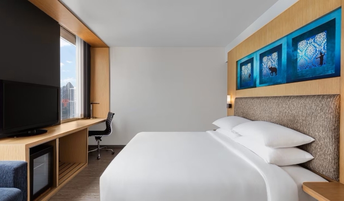 Fluffy white sheets on a double bed in front of a TV and a window showing a cityscape at the Aloft Bangkok Sukhumvit 11 hotel in Bangkok, Thailand