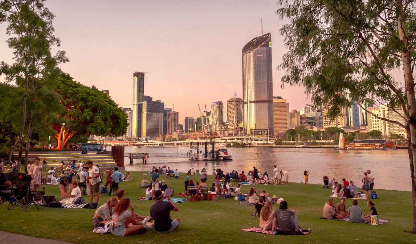 People relaxing on the edge of South Bank near the water looking over towards the CBD of Brisbane, Australia