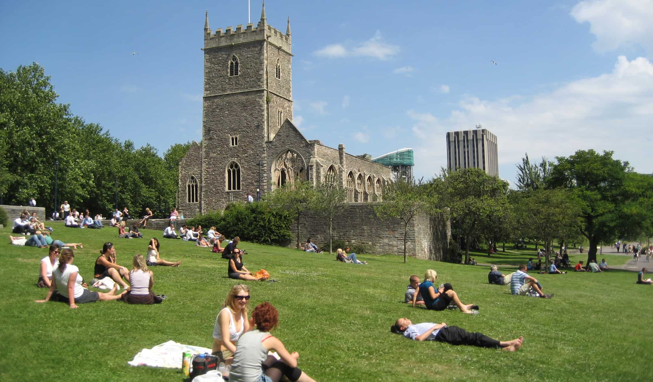 People lounging and picnicking on an expansive lawn in front of St Peter's Church in Bristol, UK