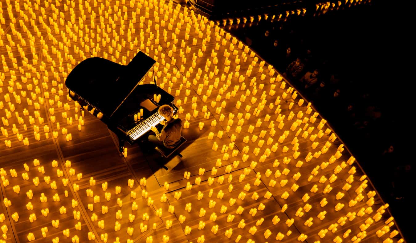 A lone grand piano on a stage entirely covered in small burning candle for a Candlelight Concert