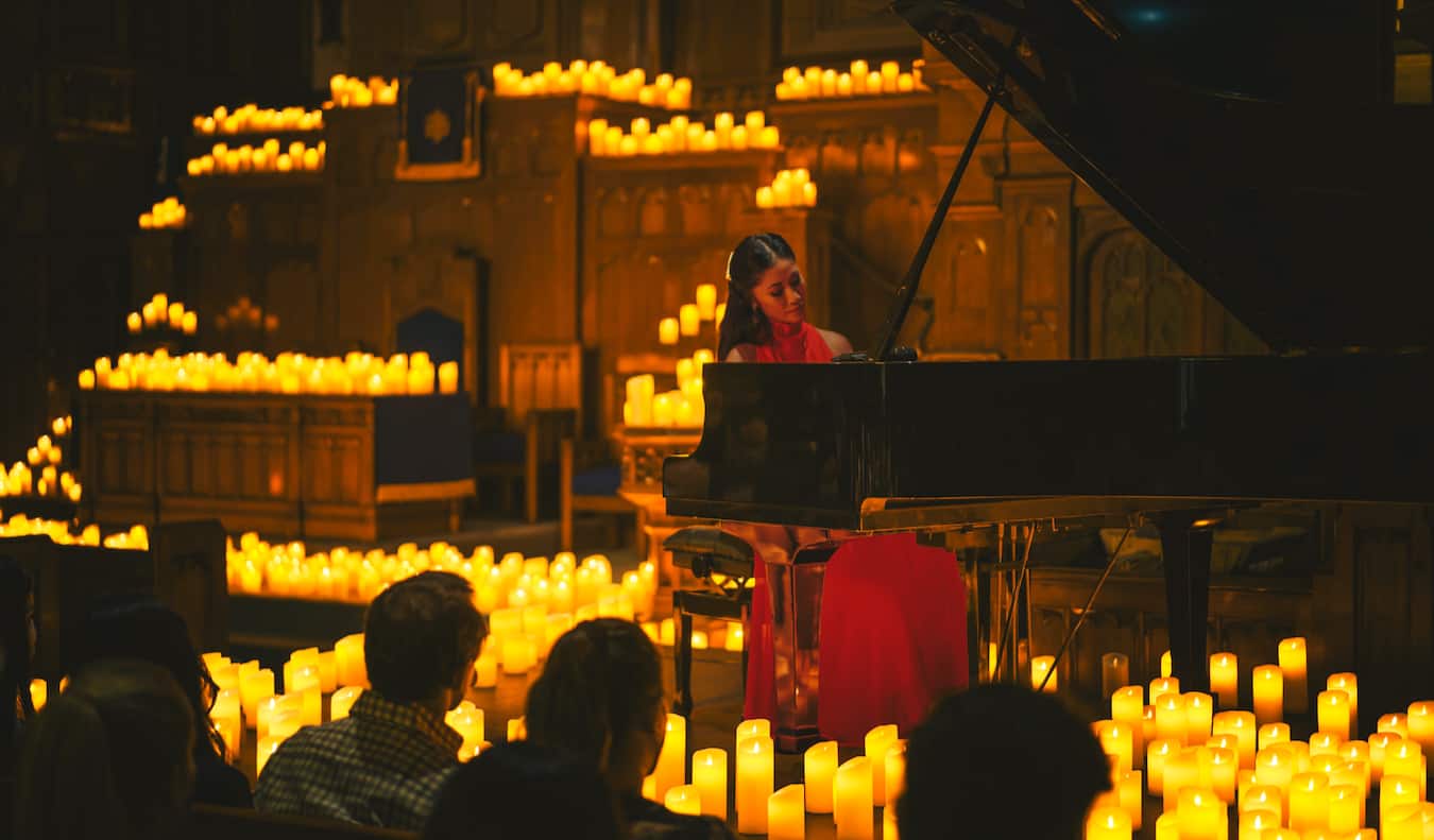 A lone woman plays the piano at a candlelight concert lit entirely by candles