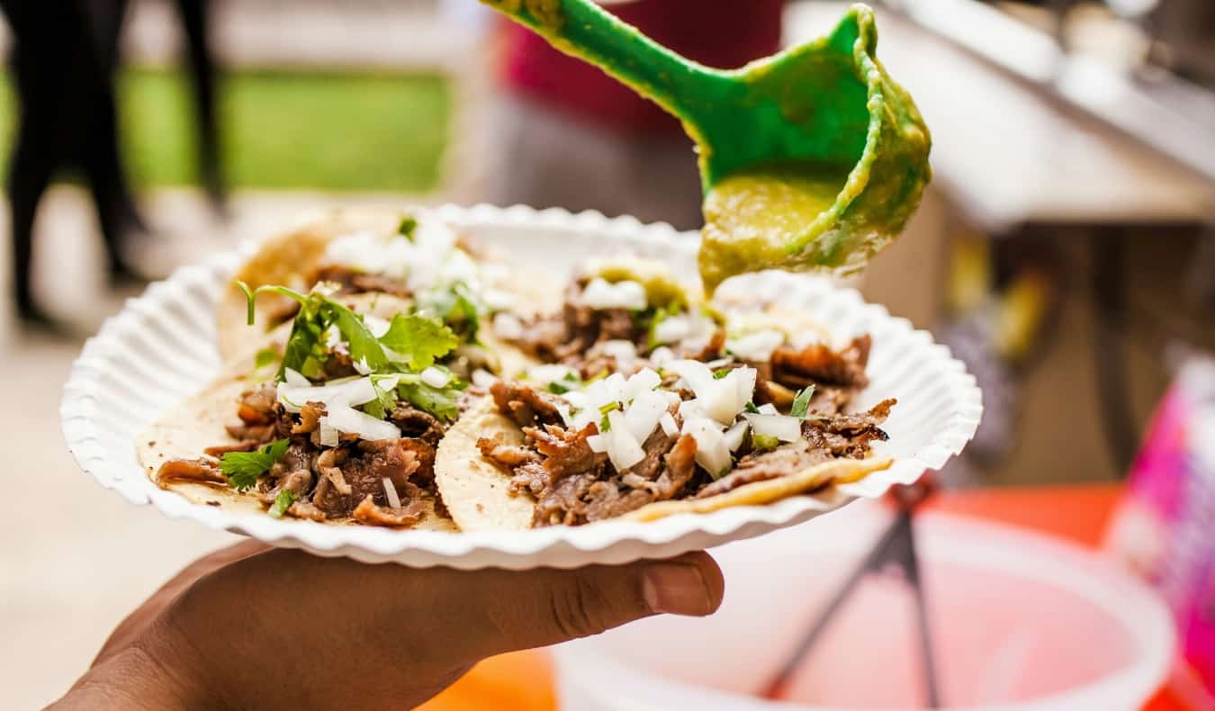 A hand holding a paper plate full of fresh tacos in Mexico City, Mexico