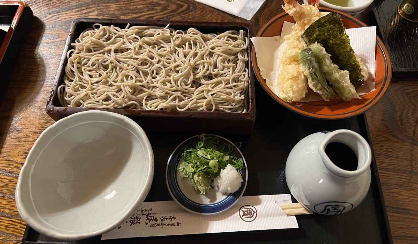 A ramen set with noodles, tempura, a pot of soy sauce, and an empty bowl at a ramen shop in Japan