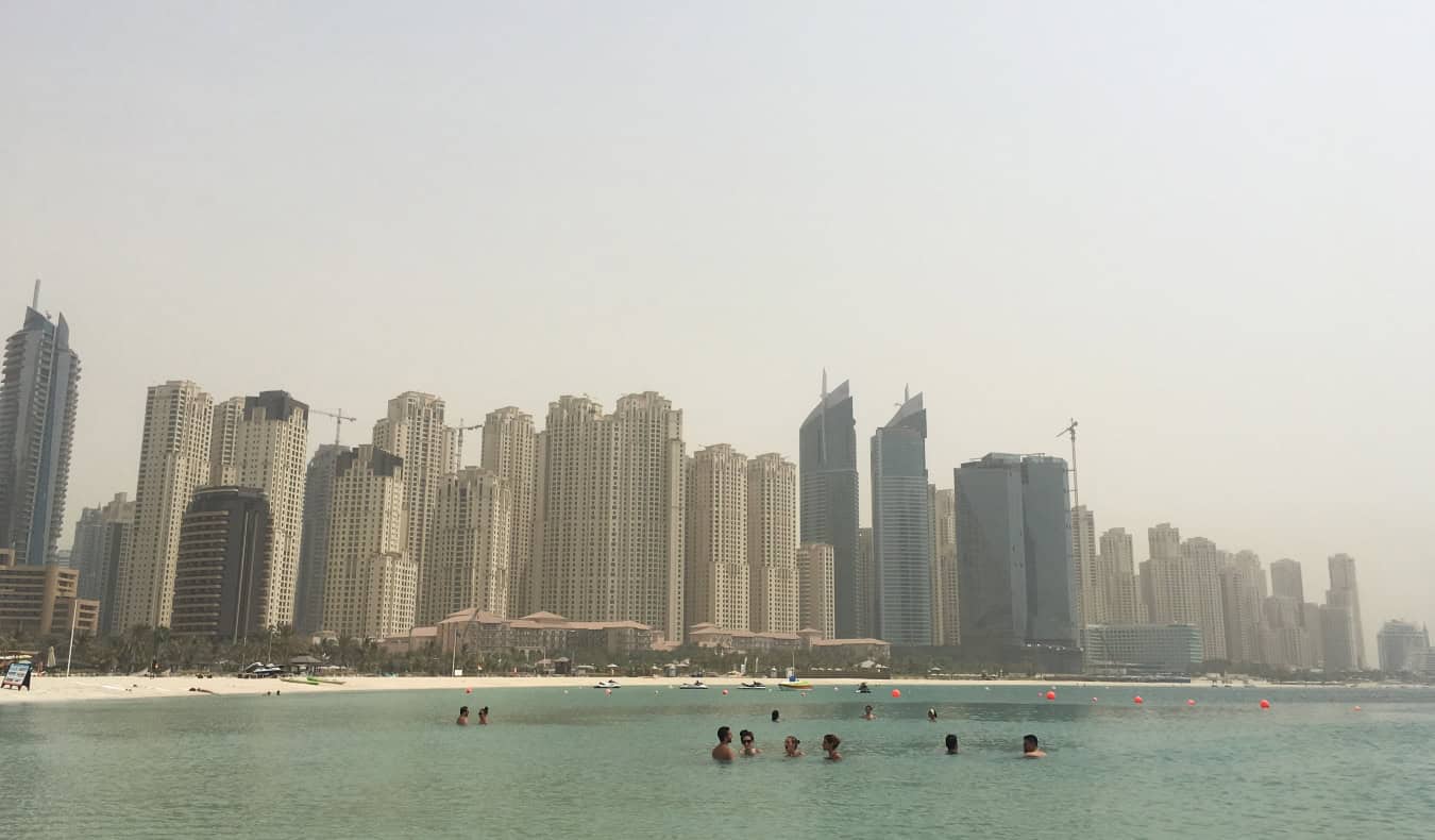 The towering skyline of downtown Dubai with people swimming in a large body of water in the foreground