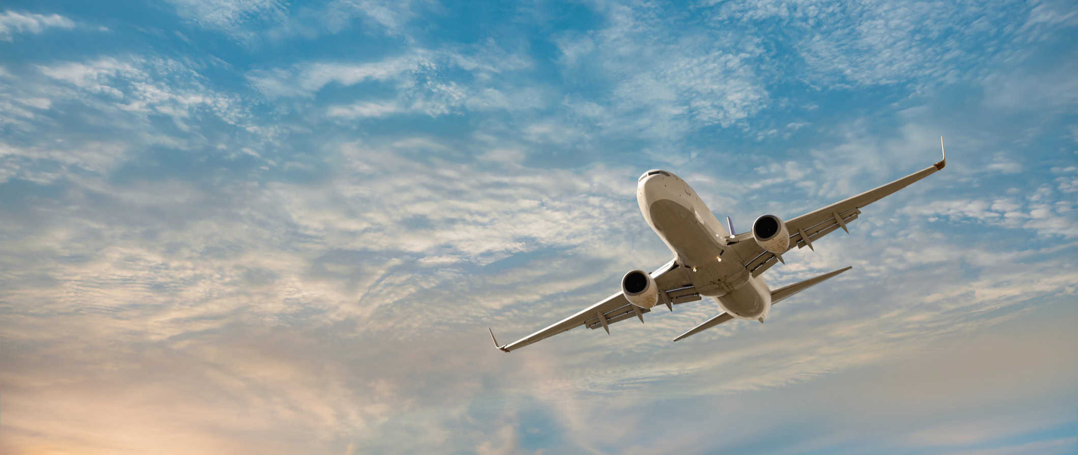 A large, commercial plane soaring through a cloudy sky with the sun in the background