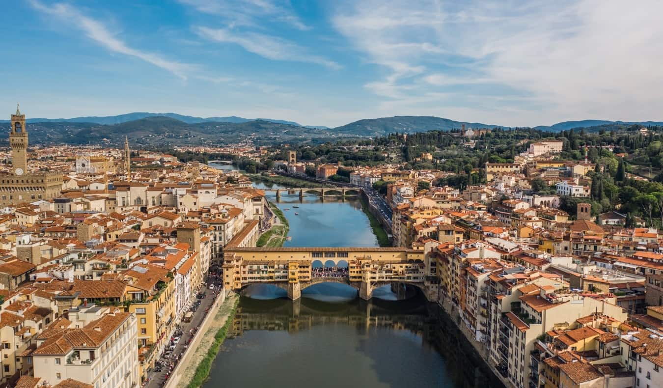 Aerial view of the city of Florence with the Ponte Vecchio in the foreground and the Arno River with mountains in the background