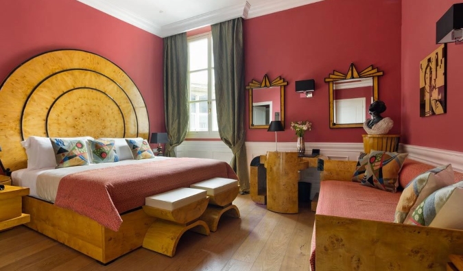 A hotel room at La Maison du Sage in Florence, Italy, with vibrant salmon-colored walls and a bed, desk, and mirror all decorated in a funky wooden Art Deco style.