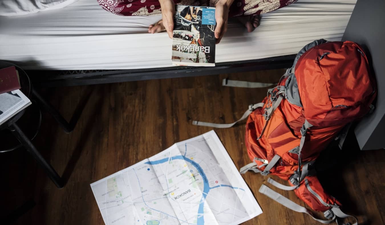 A backpack on the floor of a hostel dorm near a map in Bangkok