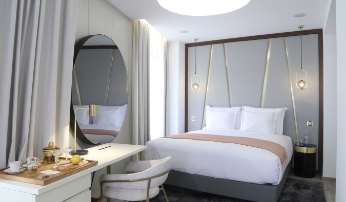 A guest room with a modern design, featuring a large round mirror above in a writing desk and a bed with hanging gold lights above it at São Vicente Alfama Hotel in Lisbon, Portugal