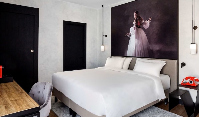 A large painting hangs above a double bed in a hotel room with a wooden desk and red rotary phone on the nightstand table at Radisson RED Madrid in Madrid, Spain