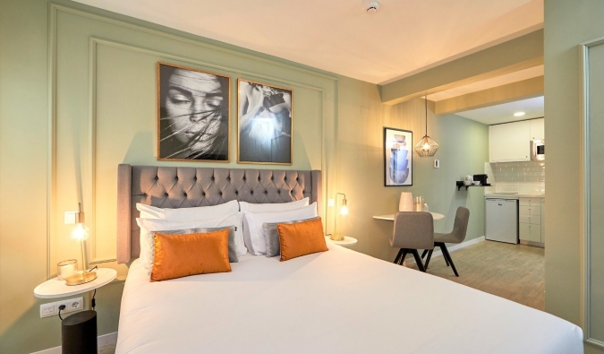 Two portrait photographs hang above a double bed in a sage-colored studio with a kitchenette and table at L&H La Latina aparthotel in Madrid, Spain