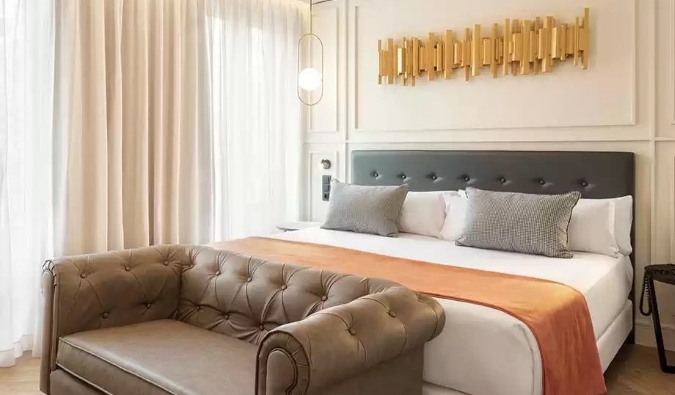 A golden piece of decor hangs above a double bed with a love seat at the foot of the bed at Hotel Catalonia Goya in Madrid, Spain