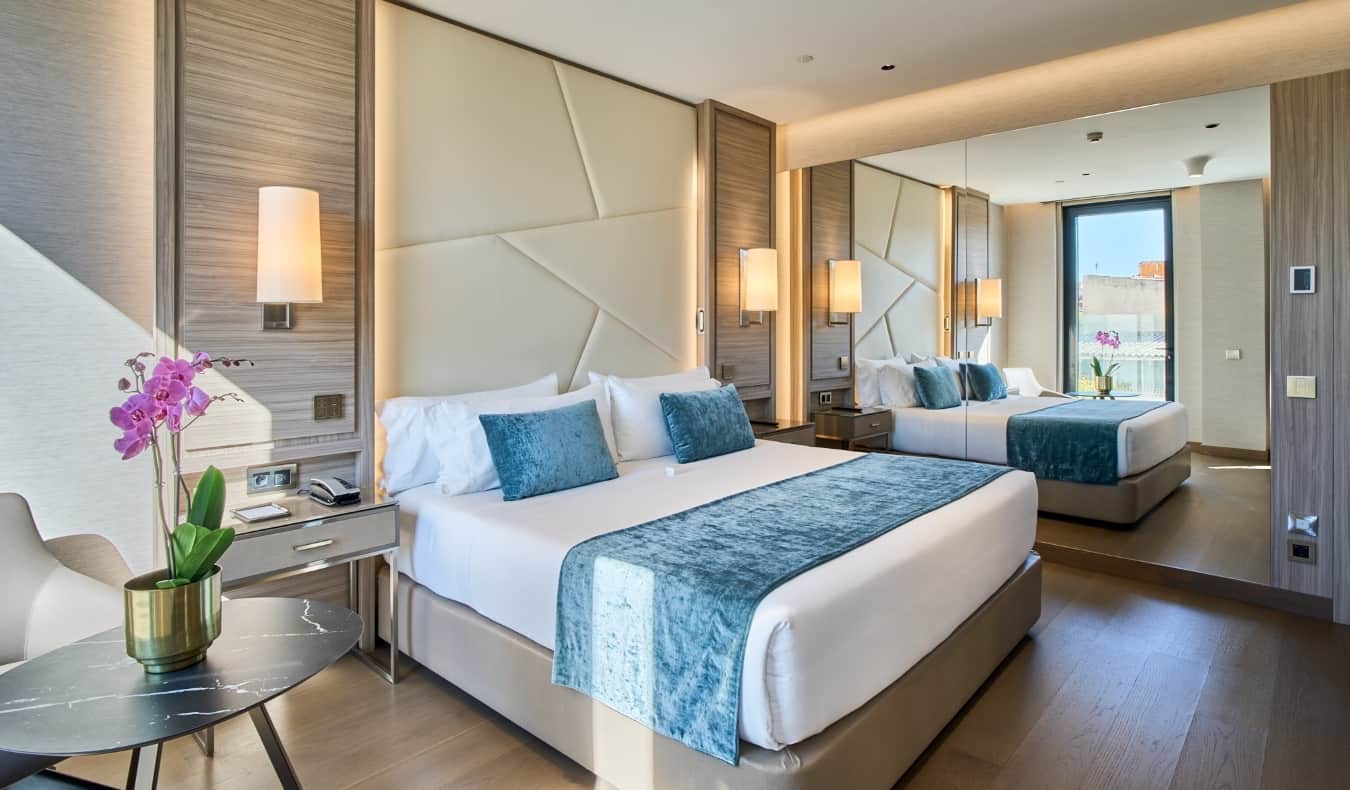 A king sized bed in a hotel room with a contemporary design, a large mirror, and orchids on the table at VP Plaza España Design in Madrid, Spain