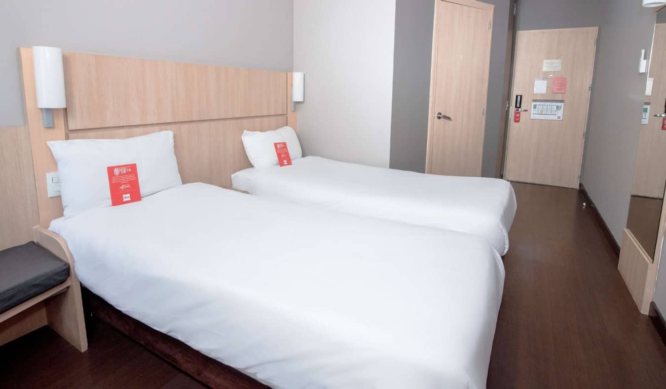 A minimal guest room with two twin beds and grey walls at the Ibis hotel in Medellin, Colombia