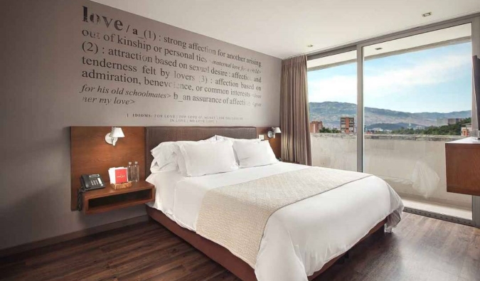 A double bed with a quote painted on the wall above it and large windows showing the skyline of Medellin, Colombia