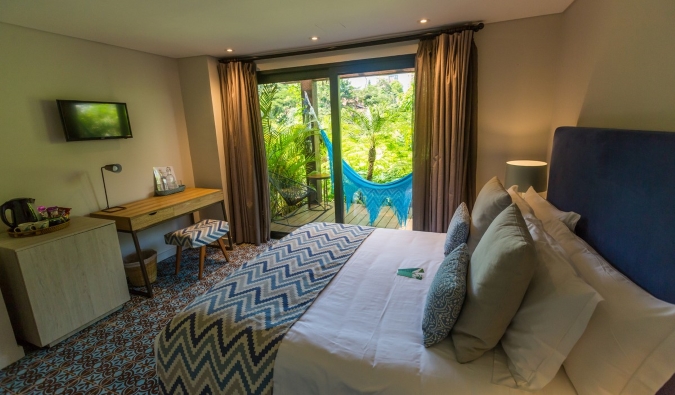 A cozy guest room with a double bed, desk, tiled floors, and sliding doors opening to a patio with a hammock at Patio del Mundo, a boutique hotel in Medellin, Colombia