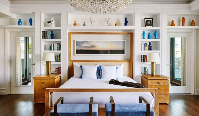 Queen sized bed with bookshelf behind covered in different pieces of artwork at The Betsy Hotel in Miami, Florida