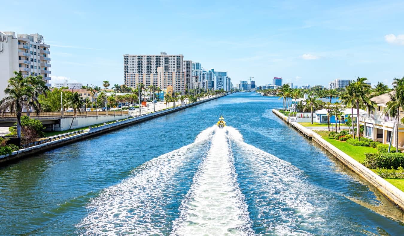A boat cruises down a large canal lined with apartment buildings and palm trees in Miami, Florida