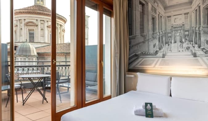 A double bed in a hotel room with an open door leading to a terrace overlooking a basilica at the B&B Hotel Milano Sant'Ambrogio, a hotel in Milan, Italy
