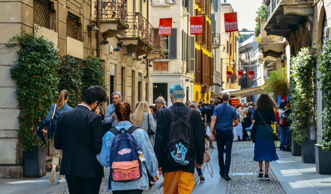 People walking up a narrow street lined by shops and cafes in bustling Milan, Italy