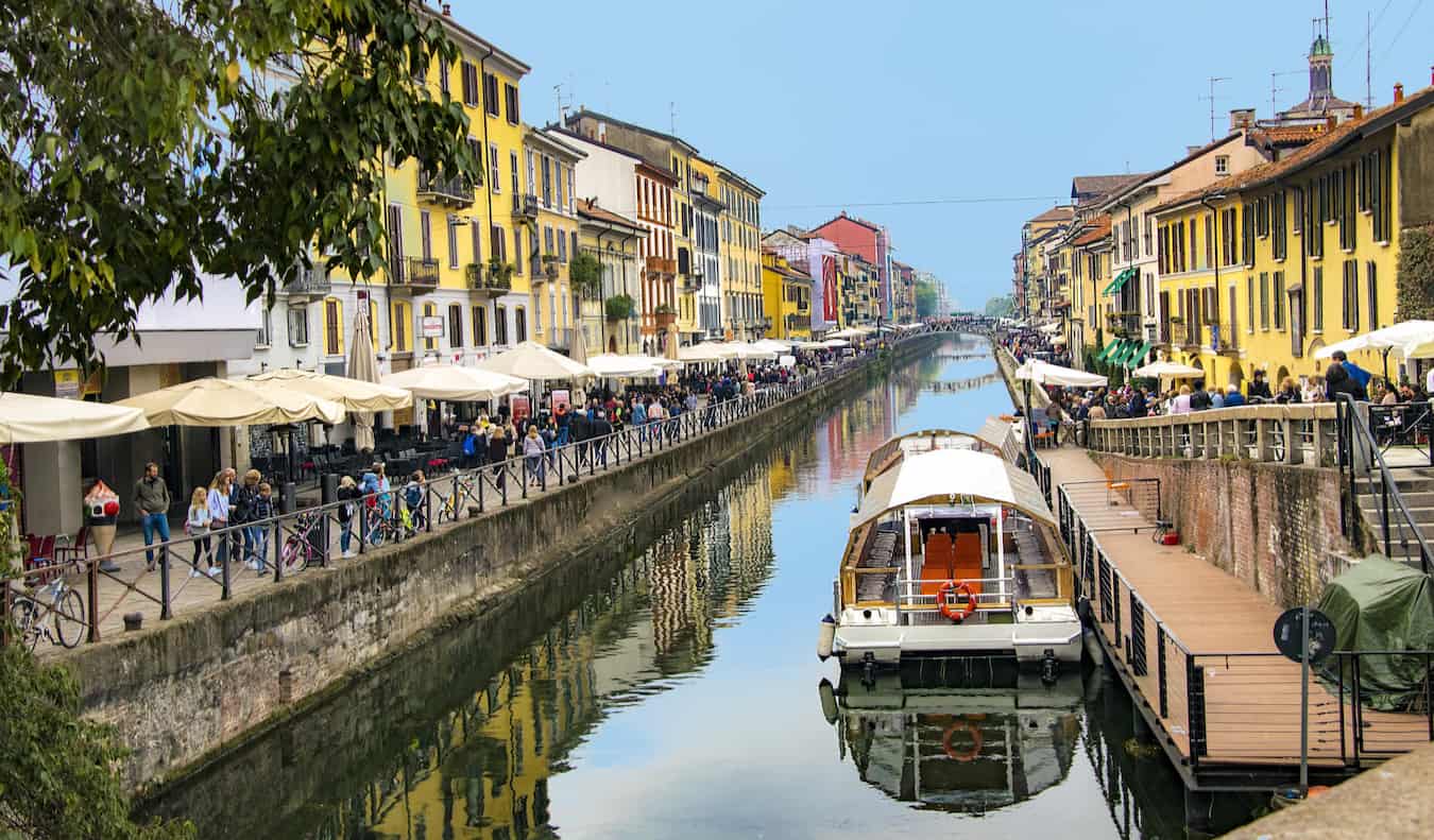 A narrow canal lined by busy cafes and restaurants in sunny Milan, Italy
