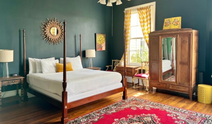 Um quarto de hóspedes com paredes verde-escuras, piso de madeira, cama de dossel, guarda-roupa de madeira e grandes janelas no Creole Gardens Inn, um hotel em Nova Orleans, Louisiana