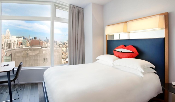 A hotel room with a pillow in the shape of lips on the crisp white queen bed at The Standard hotel in NYC