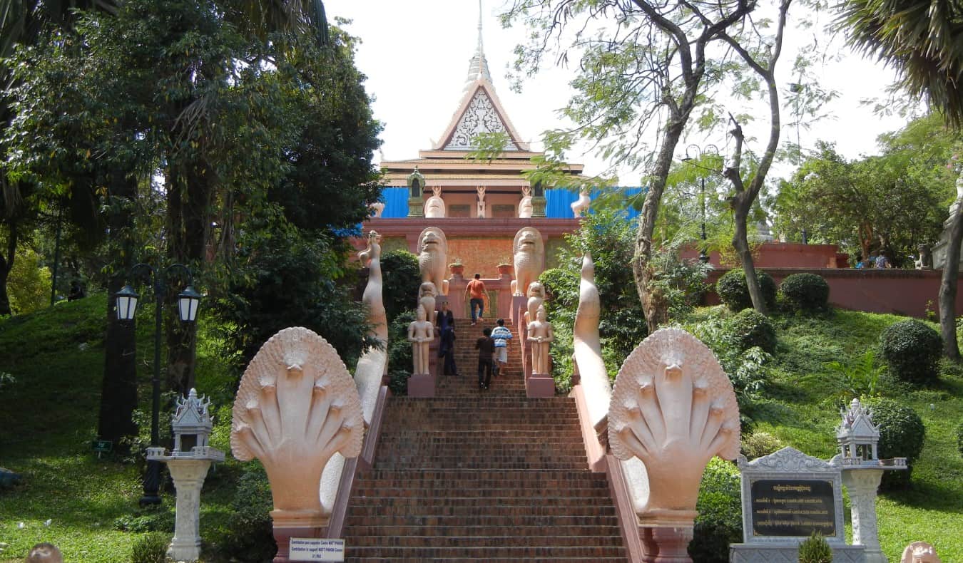 A tall staircase surrounded by trees and statues leading up to Wat Phnom Daun Penh Buddhist temple in Phnom Penh