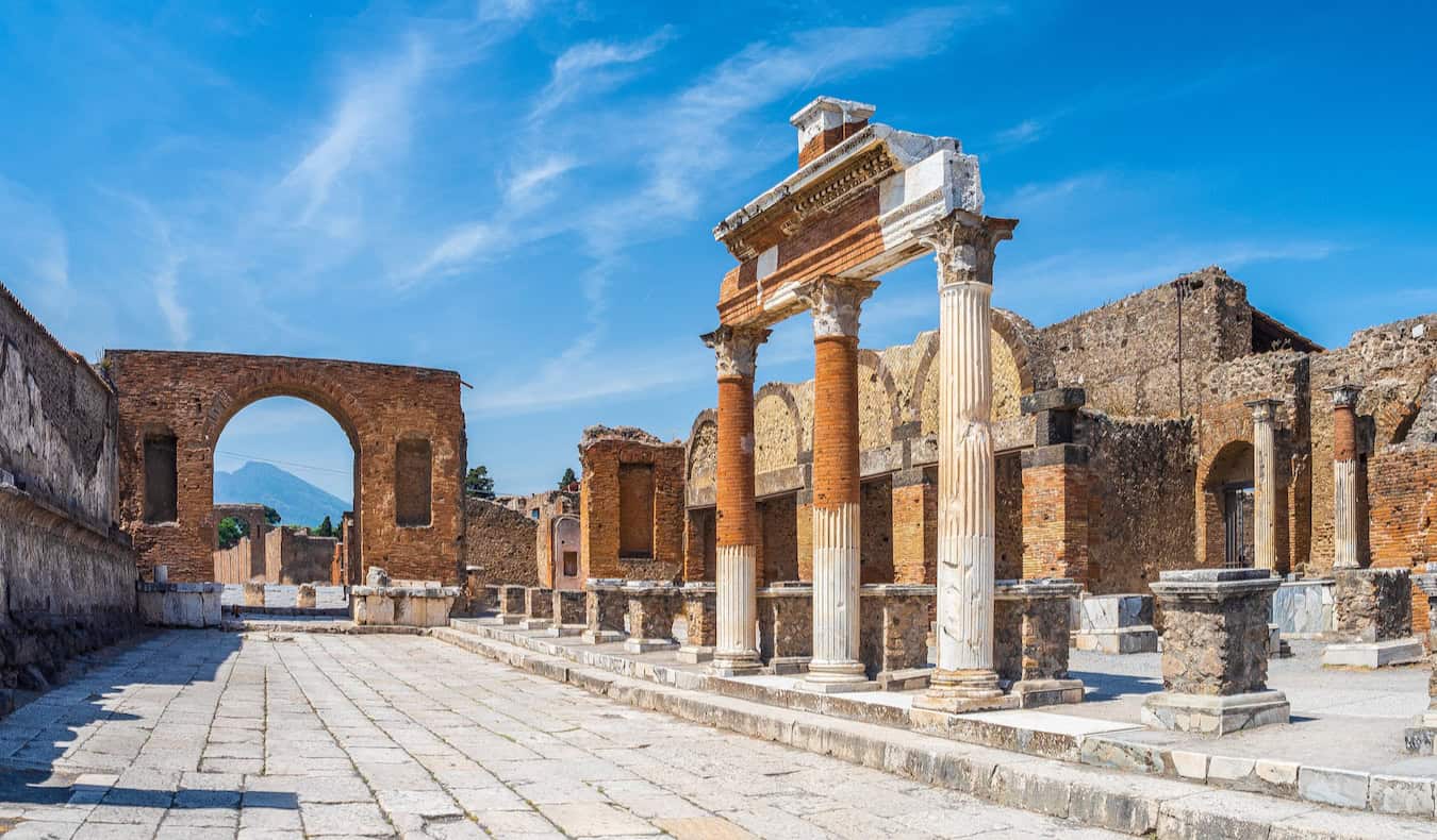 Cobblestone street in Pompeii lined with the ancient ruins of buildings on a bright and sunny day in Italy