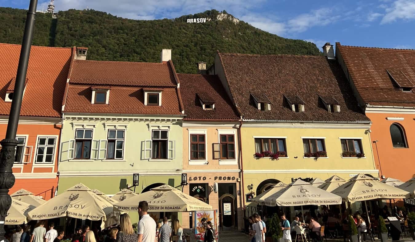 Colorful houses in a row along a square with a huge 'Brasov' sign embedded in the hills above the town of the same name in Romania