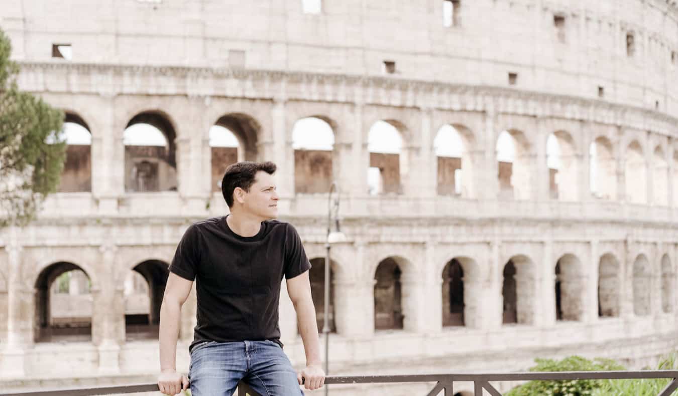 Nomadic Matt posing for a photo near the massive and ancient Roman Colosseum in Rome, Italy