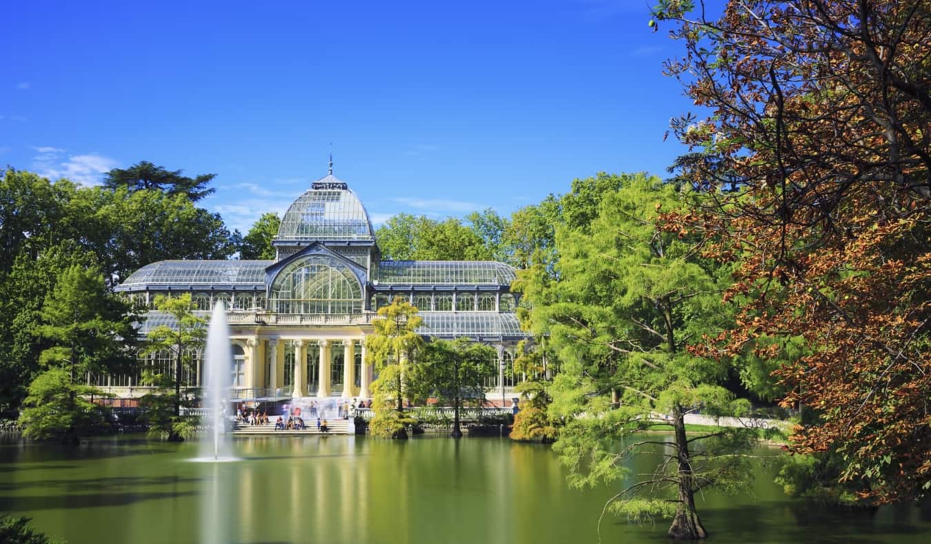 The glass Crystal Palace overlooking a small pond surrounded by trees in El Retiro Park in Madrid, Spain