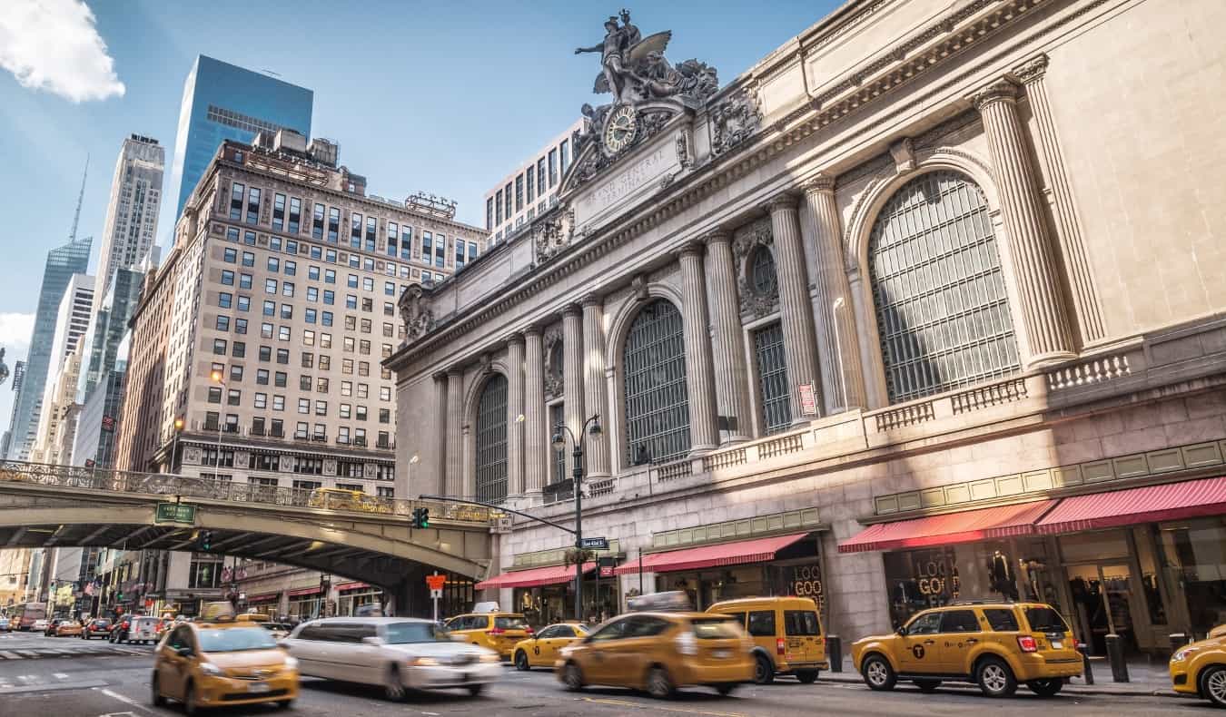 The exterior of Grand Central Terminal with many yellow taxis going down the street in front of it in New York City