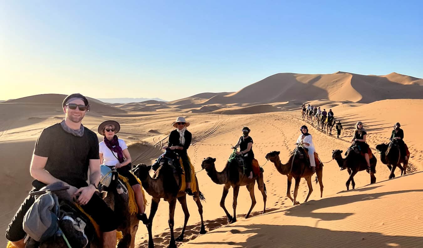 A TNN group tour in Morocco riding camels together in the sprawling arid desert