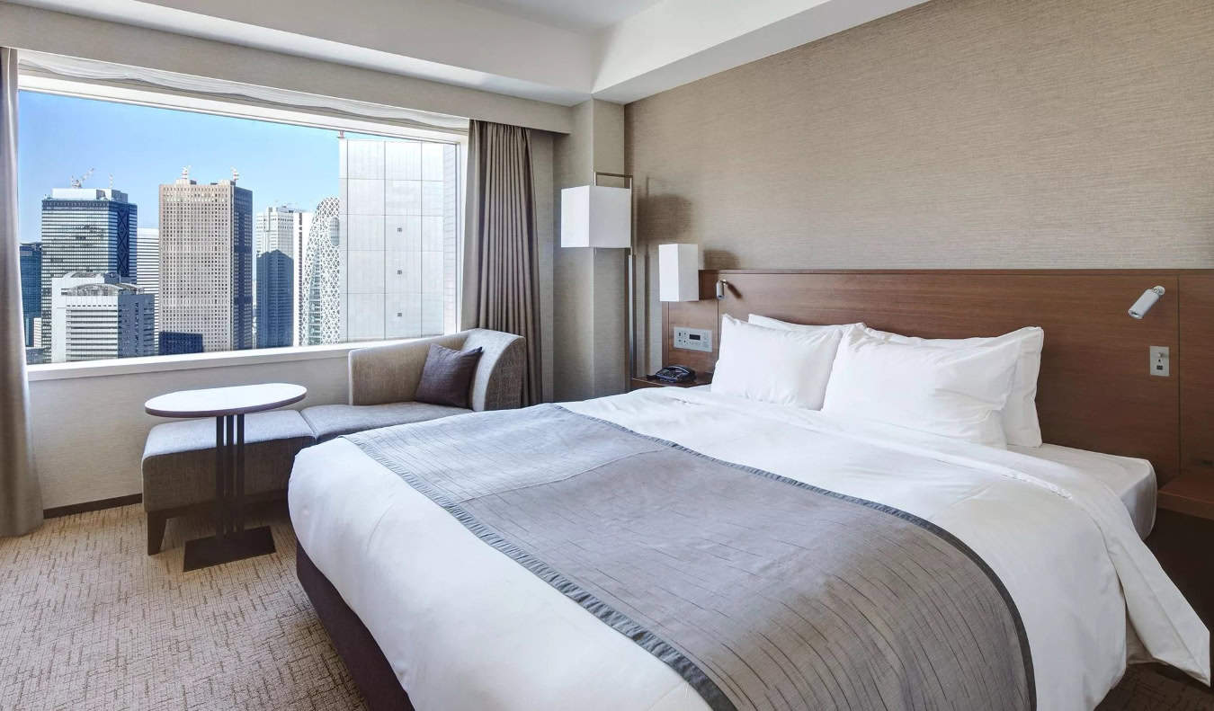 A hotel room with a double bed and a large window overlooking the skyline of Tokyo, Japan
