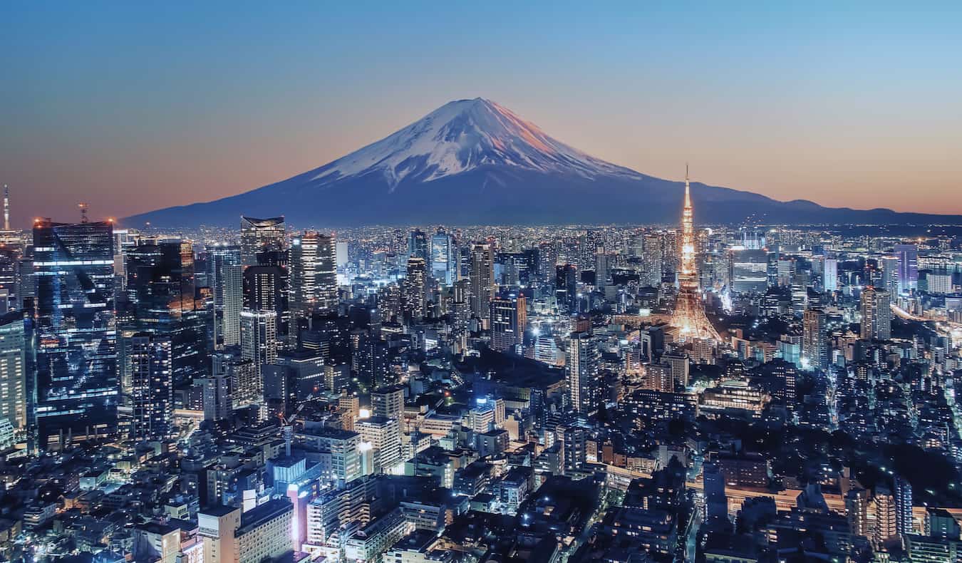 The sprawling skyline of Tokyo, Japan lit up at night with Mount Fuji in the distance