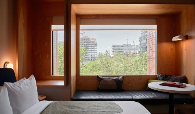 A bed in front of a picture window in a wood-paneled wall, with a window bench in front of it at the Ace Hotel in Toronto, Canada