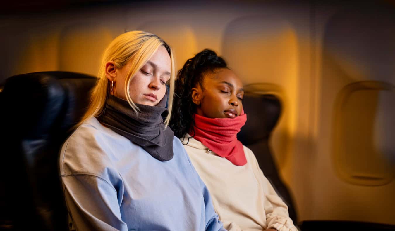 Two women using Trtl travel pillows during their long-haul flight