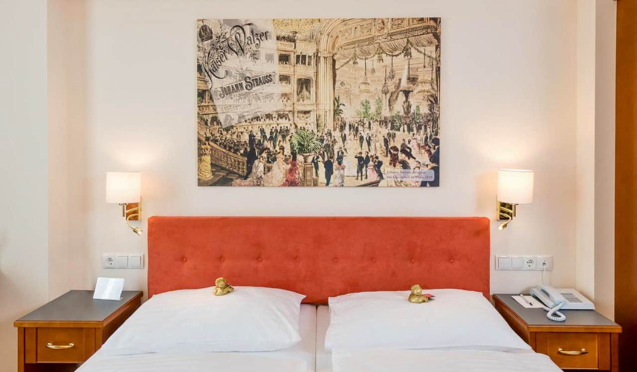 A large, comfy bed with artwork above it at Hotel Johann Strauss in Vienna, Austria