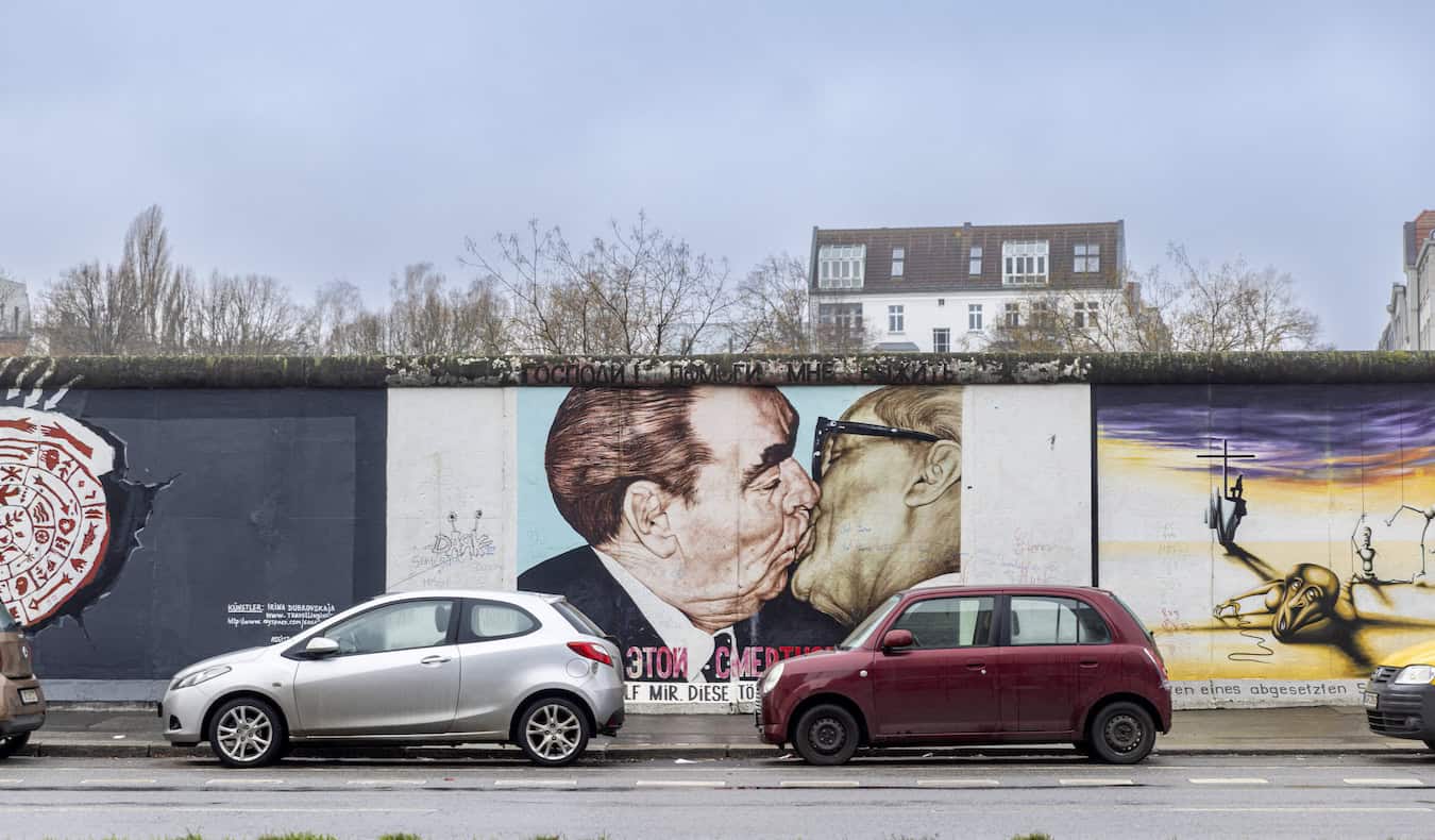 A person biking past a colorful mural at the East Side Gallery in Berlin, Germany
