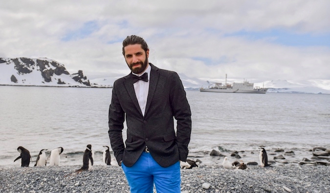 Jon Levy posing for a photo in Antarctica with penguins nearby