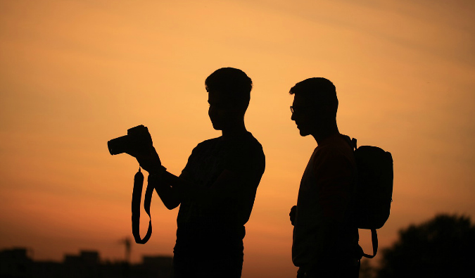 Two photographers at sunset looking at a camera as they take photos