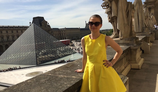 A solo female traveler in a yellow dress posing in front of the Louvre, Paris