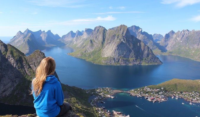 Female traveler sitting on transcend of a mount staring onto the body of body of water overseas 6 Women Who Conquered Personal Mountains to Travel the World