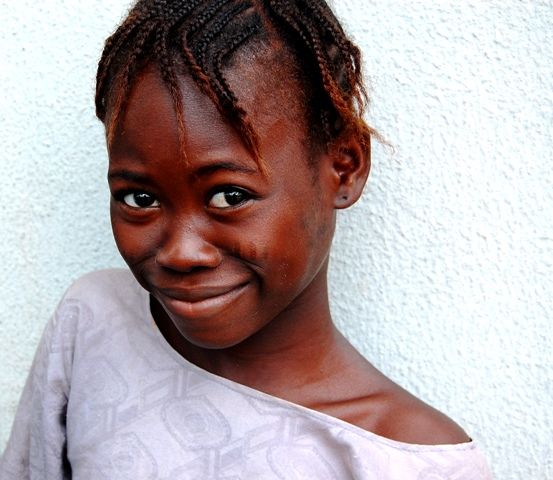A young black girl standing near a white wall posing