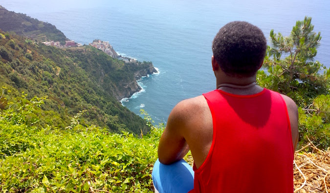 A solo male traveler sitting on a cliff enjoying the view over the ocean